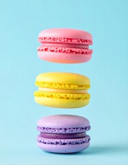 Colorful macarons float mid-air on pastel blue background. Pink, yellow, purple, and turquoise cookies in soft light. Minimal, playful, elegant dessert display.