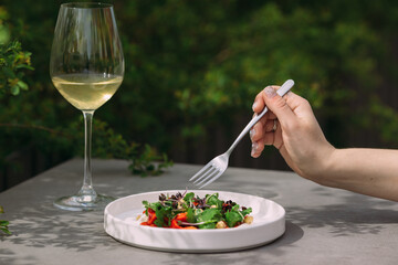 Woman eating fresh salad with white wine outdoors