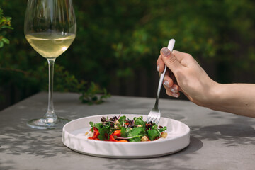 Person eating fresh green salad with white wine