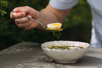 Hand holding spoonful of green soup and boiled egg