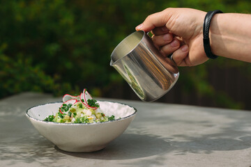 Hand pouring liquid from metal pitcher into okroshka