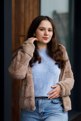 A girl in blue jeans and a warm jacket against the background of a bench.