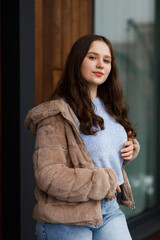 A girl in blue jeans and a warm jacket against the background of a bench.