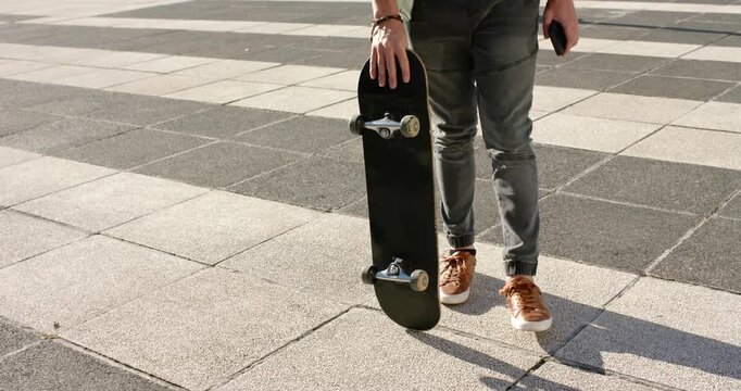 Man holding board and phone on large tiled plaza leaning in stepping forward to cross plaza
