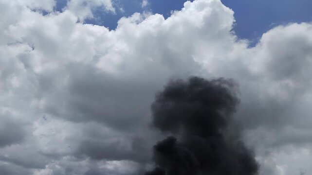 Un primer plano de un cielo azul con unas nubes blancas rodeado de un fuerte humo negro