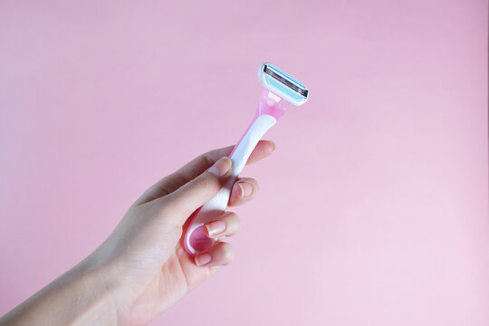 Woman hand holding razor in front of pink background.