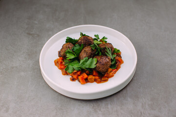 Meatballs with vegetables on white plate on grey background