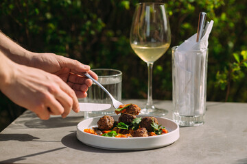 Person eating meatballs and vegetables at outdoor restaurant