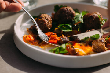 Person eating meatballs and vegetables at restaurant