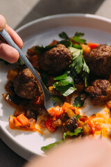 Person eating meatballs with vegetable ragout and fresh parsley