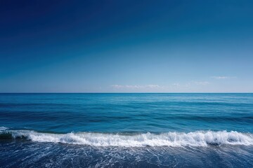 Naklejka premium Gentle ocean waves lap against a serene deep blue water under a clear sky, creating a peaceful atmosphere at a quiet seaside location