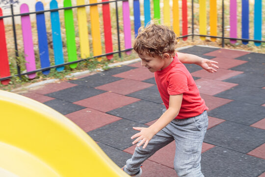 A cheerful child in a red shirt captured in dynamic motion while playing on a colorful playground