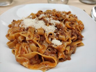 A delicious plate of fresh Italian pappardelle or tagliatelle pasta, richly coated in a hearty meat ragu sauce and topped with grated Parmesan cheese, served in Italy.