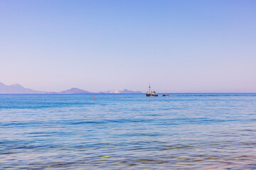 Fishing boat sailing on background of blue Aegean Sea with distant islands and clear summer sky. Greece. Kos.