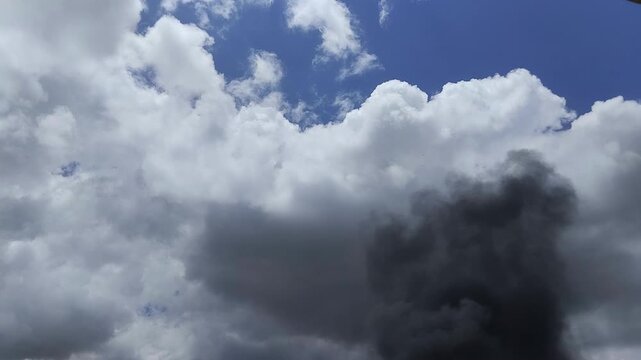 Un primer plano de un cielo azul con unas nubes blancas rodeado de un fuerte humo negro