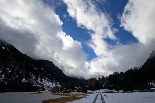 Valle de monta&ntilde;a cubierto de nieve con un sendero que avanza entre laderas oscuras, bajo un cielo azul con nubes que aportan luz y profundidad al paisaje invernal.