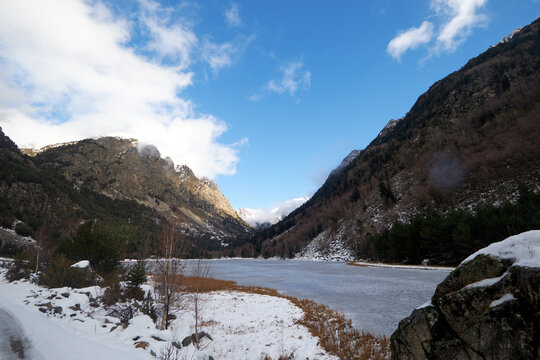 Valle de monta&ntilde;a con nieve y un tramo de agua helada entre laderas rocosas, bajo un cielo claro que ilumina las cumbres al fondo.