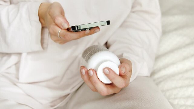 Woman using her mobile phone to search details about her pills medication. Research reading information about vitamins supplements online, side effects or benefits, health care application.