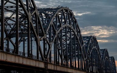Obraz premium A railway bridge spanning over a river at sunset, with warm golden light reflecting on the water.