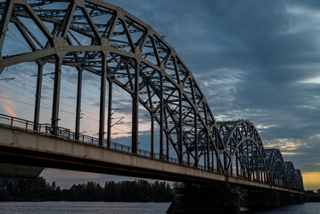 A railway bridge spanning over a river at sunset, with warm golden light reflecting on the water.