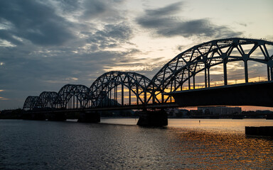 A railway bridge spanning over a river at sunset, with warm golden light reflecting on the water. 