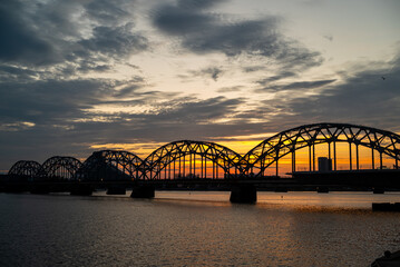 A railway bridge spanning over a river at sunset, with warm golden light reflecting on the water. 