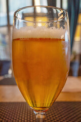 close up of a glass of beer with a foamy head, sitting on a brown surface