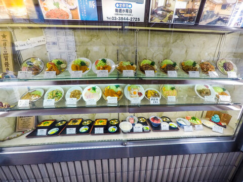 Vitrina con r&eacute;plicas de comida japonesa en pl&aacute;stico, mostrando platos individuales y men&uacute;s completos con carteles y fotos promocionales. Escena t&iacute;pica de restaurante en Jap&oacute;n.