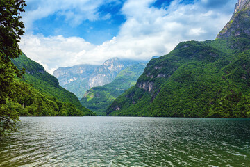 Serene landscape featuring a tranquil lake  Mis surrounded by lush green Dolomites  in Italy  mountains under a bright blue sky with fluffy clouds, showcasing the beauty of nature  © Nizoli