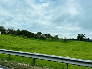 Green rolling hills and a village house along a German countryside road under a cloudy sky