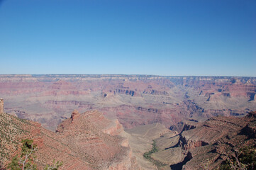 Panoramic view of the Grand Canyon with layered red rock formations, steep cliffs, and wide valleys beneath a clear blue desert sky