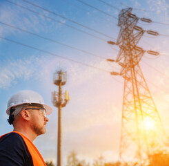 Male electrical engineer stands next to power lines and a 5G mobile communication tower against the backdrop of the sunset and blue sky. Power management.