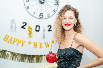 Cheerful woman in elegant dress holding festive drink and smiling during New Year’s Eve...