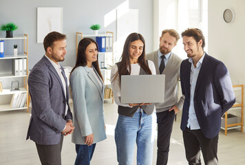 Young smiling business woman showing work project to colleagues on a laptop computer standing in...
