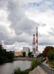 Obraz premium Smoke stacks rise above riverside industrial area under cloudy sky