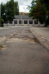 Obraz premium Empty street with old tram tracks and worn pavement near a building in the city during a cloudy day