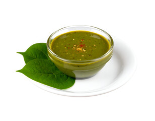 A vibrant green sauce served in a glass bowl garnished with spices and fresh leaves on a white plate.