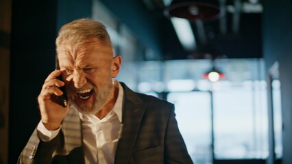 Senior manager arguing smartphone walking sunlit corridor closeup. Furious man