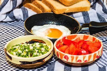 Close up of fried egg in a small frying pan  and different bowls with copped vegetables in a rustic composition