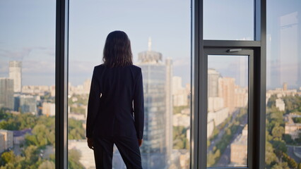 Successful manager contemplating cityscape from office panoramic window.