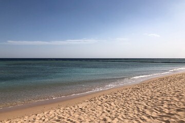 Turquoise water gently meeting a sandy beach under a clear sky.  A peaceful seaside scene with gentle waves lapping the shore under the summer sun