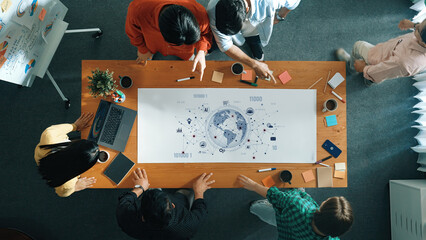 A diverse team collaborates around a wooden table, engaging in strategic discussions. The world map and planning tools highlight a dynamic modern office environment. Trope