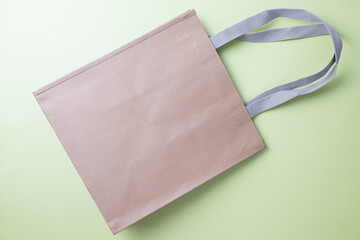 Reusable, washable brown paper shopping bag with gray cloth handles on green background.