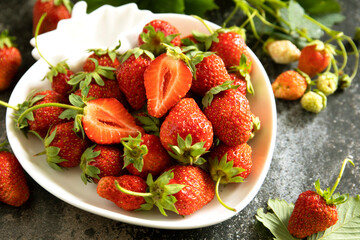 Fresh summer strawberries in white bowl on dark rustic surface.