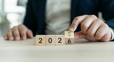 A person in a suit changes a wooden block from "5" to "6," completing the year "2026," symbolizing a business transition.