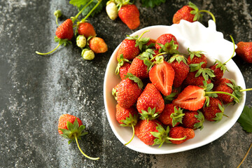 Fresh summer strawberries in white bowl on dark rustic surface. Copy space.