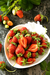 Fresh summer strawberries in white bowl on dark rustic surface.