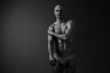 Fototapeta premium Black and white image of a confident man showcasing his toned physique. The dramatic lighting accentuates his strong features, conveying strength and determination.