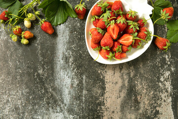 Fresh summer strawberries in white bowl on dark rustic surface.