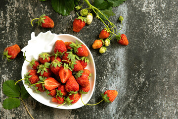 Fresh summer strawberries in white bowl on dark rustic surface.
